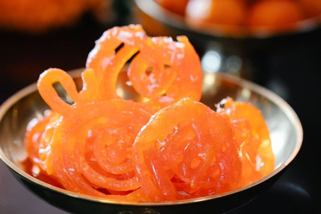 Jalebis piled in a brass bowl, with more sweets in a second bowl behind. Illustrative photograph.