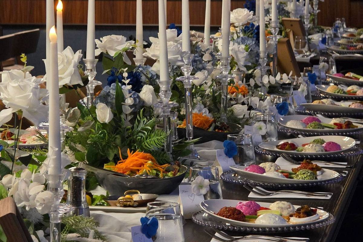 A long candlelit banquet table set with white flowers and individual plates of dips, salad and grilled vegetables. Illustrative photograph.