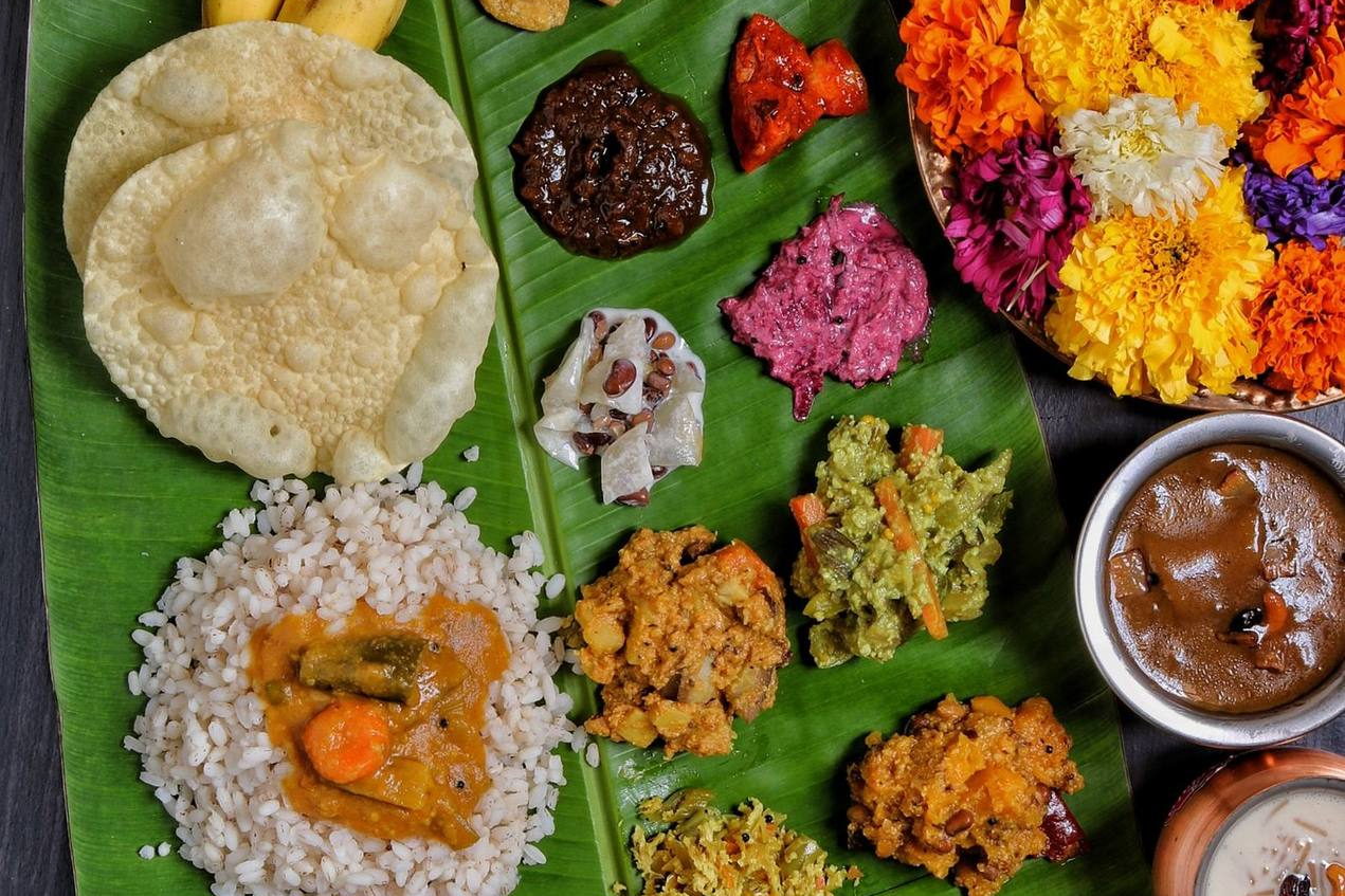 A South Indian meal laid out on a banana leaf with rice, curries, pickles and papad, a tray of flowers beside it. Illustrative photograph.