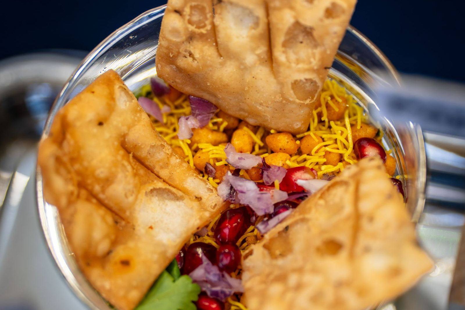 A close view of papdi chaat in a glass bowl, with crisp papdi, sev, pomegranate seeds and chopped onion. Illustrative photograph.