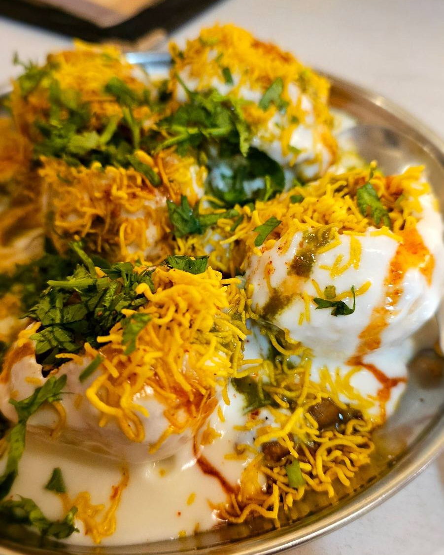A steel plate of dahi puri topped with yogurt, green and tamarind chutneys, fine sev and chopped coriander. Illustrative photograph.