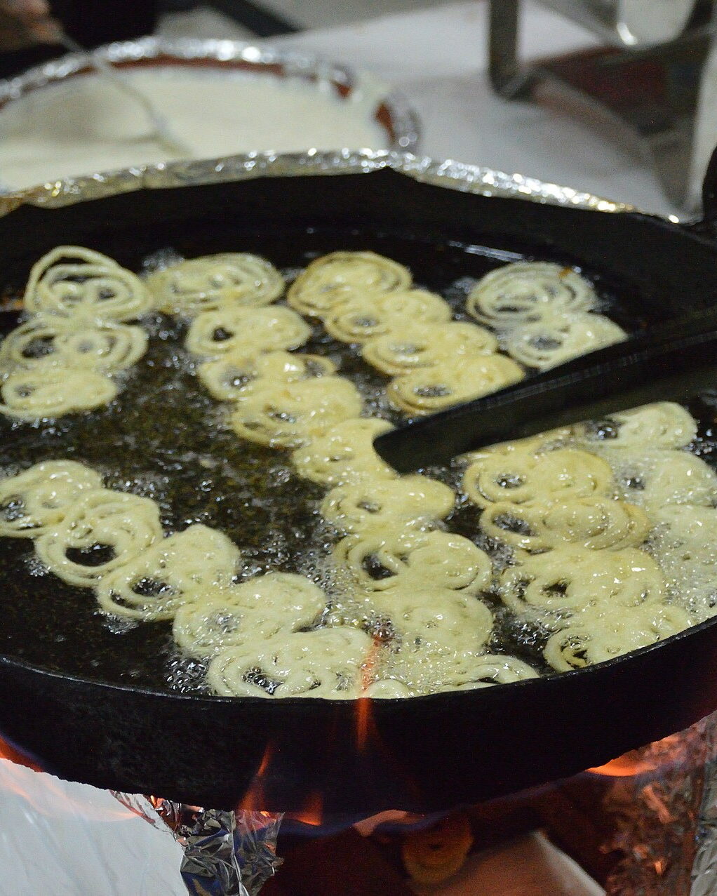 Jalebis frying in a wide pan of hot oil set over a flame. Illustrative photograph.