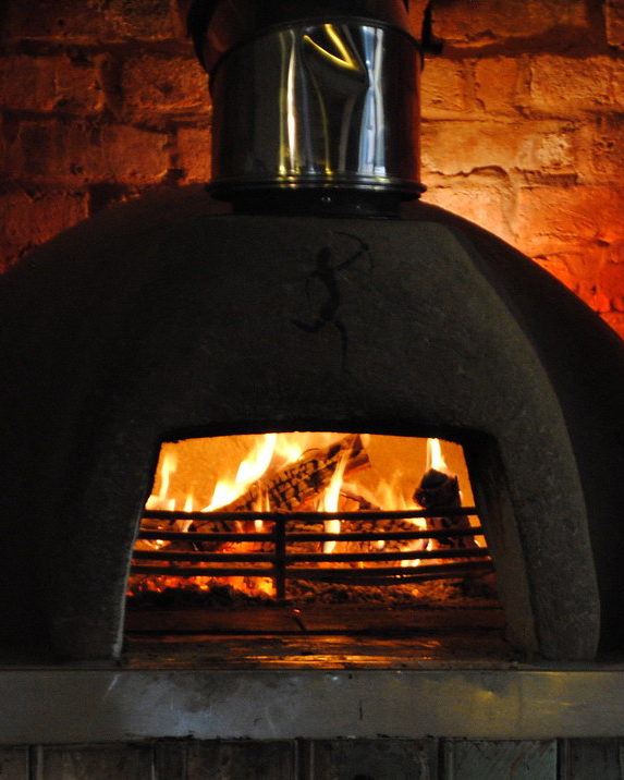 A domed wood-fired oven with a log fire burning inside its brick-lined mouth. Illustrative photograph.