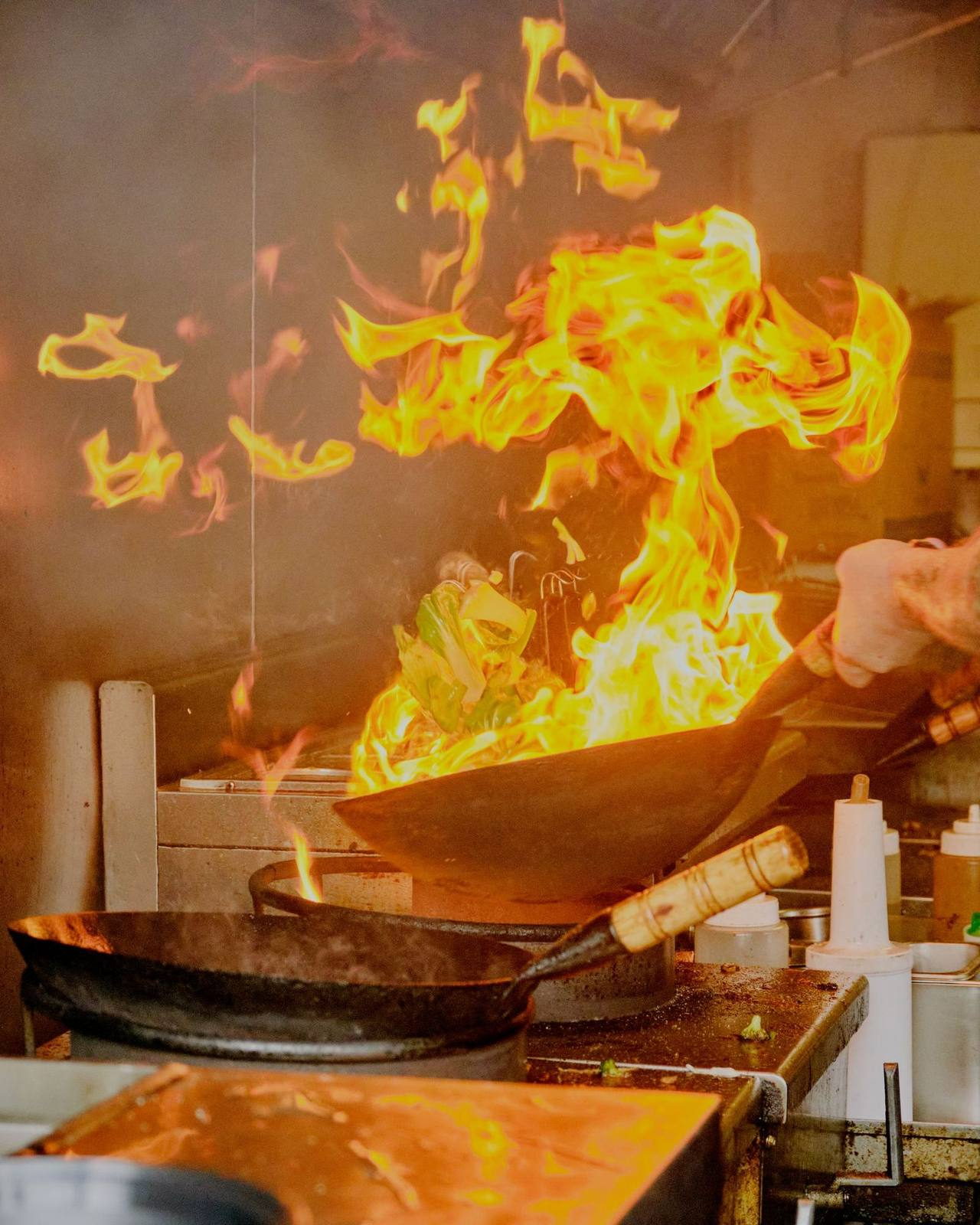 A cook tossing leafy greens in a wok as flames leap up from the burner. Illustrative photograph.
